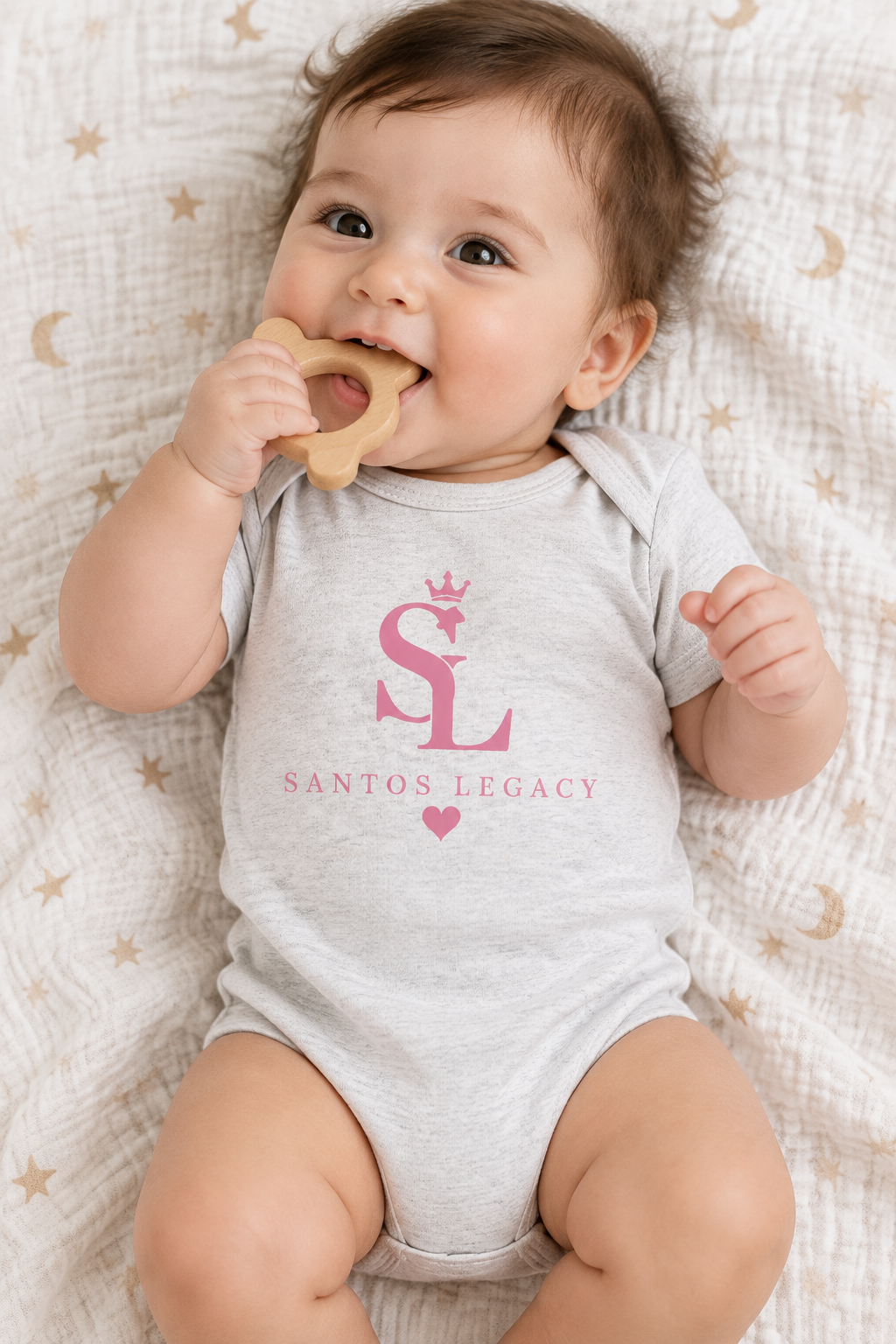 Baby wearing the Santos Legacy Baby jersey bodysuit on a muslin play blanket chewing a wooden teether