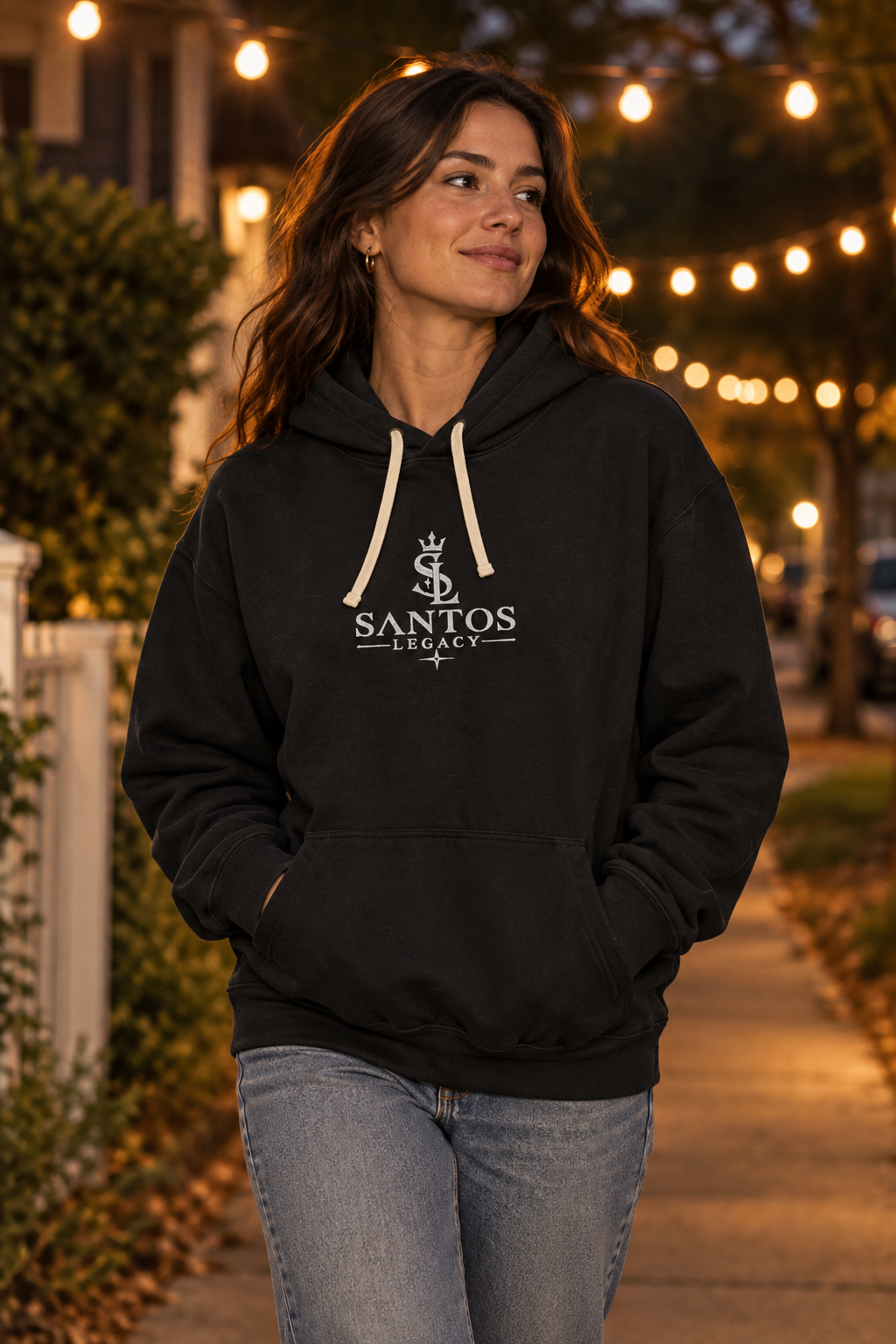 Woman wearing the Santos Legacy Signature Premium Unisex garment-dyed lightweight hoodie on an evening walk under string lights