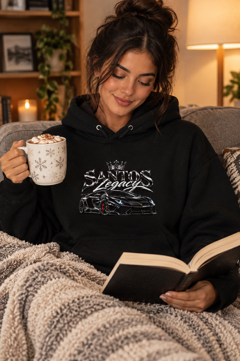 Woman wearing the Santos Legacy Signature Premium Unisex Hoodie reading on a cozy couch with cocoa