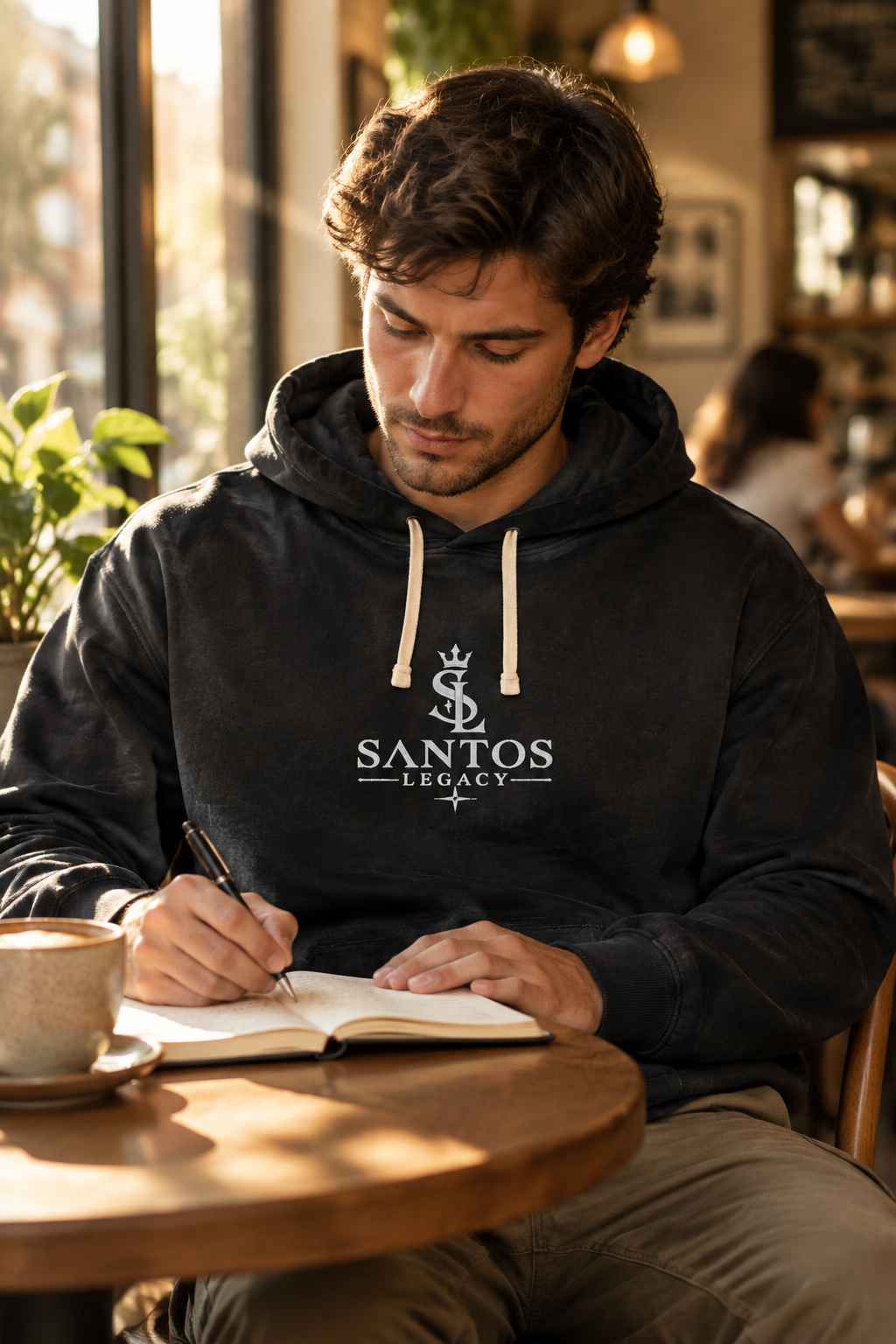 Man wearing the Santos Legacy Signature Premium Unisex garment-dyed lightweight hoodie writing in a journal at a cafe