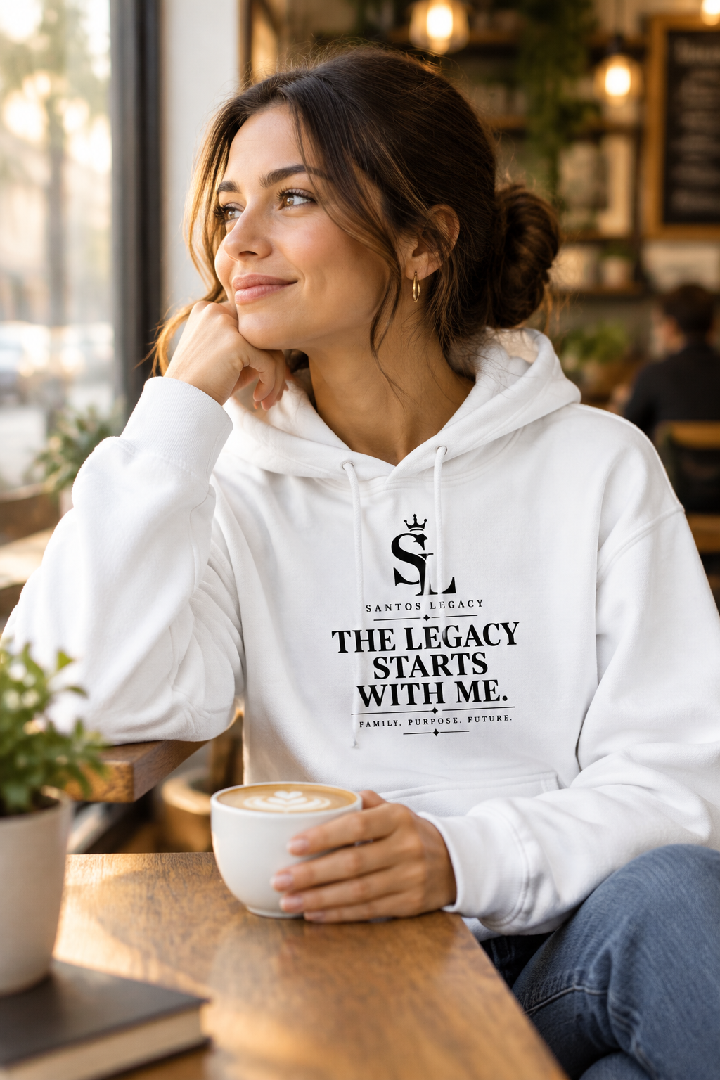 Woman wearing the Santos Legacy Signature Premium Phrase Hoodie in a cozy coffee shop
