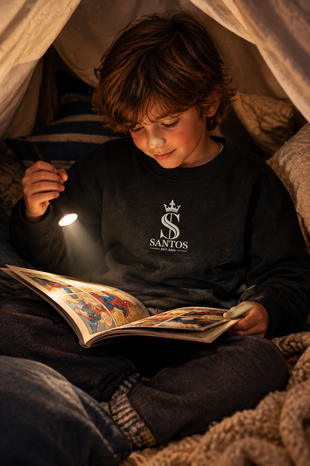 Kid wearing the Santos Legacy Signature Premium Kids crew neck sweatshirt reading a comic book in a pillow fort