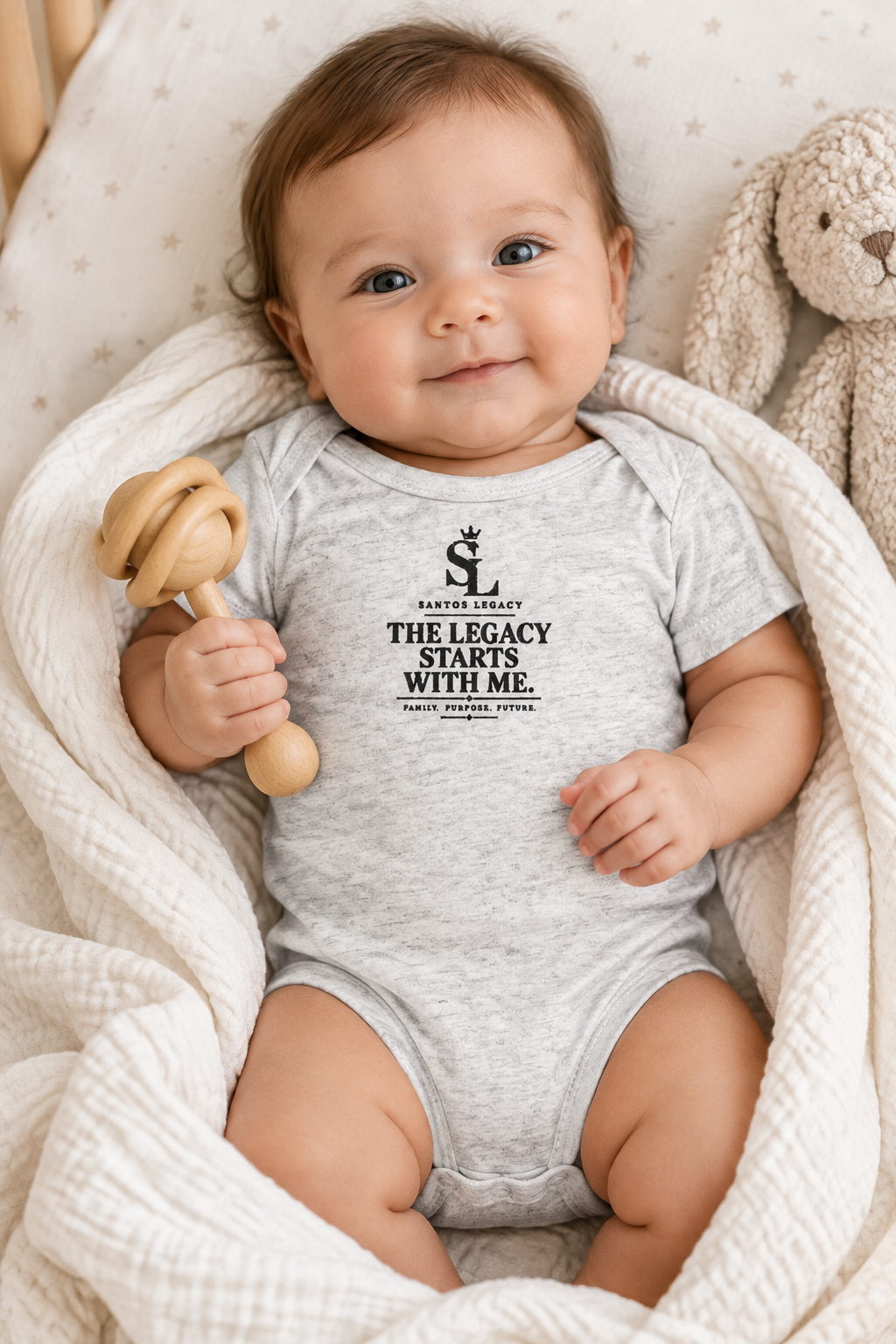 Baby wearing the Santos Legacy Little Legacy Baby jersey bodysuit wrapped in a swaddle holding a wooden rattle